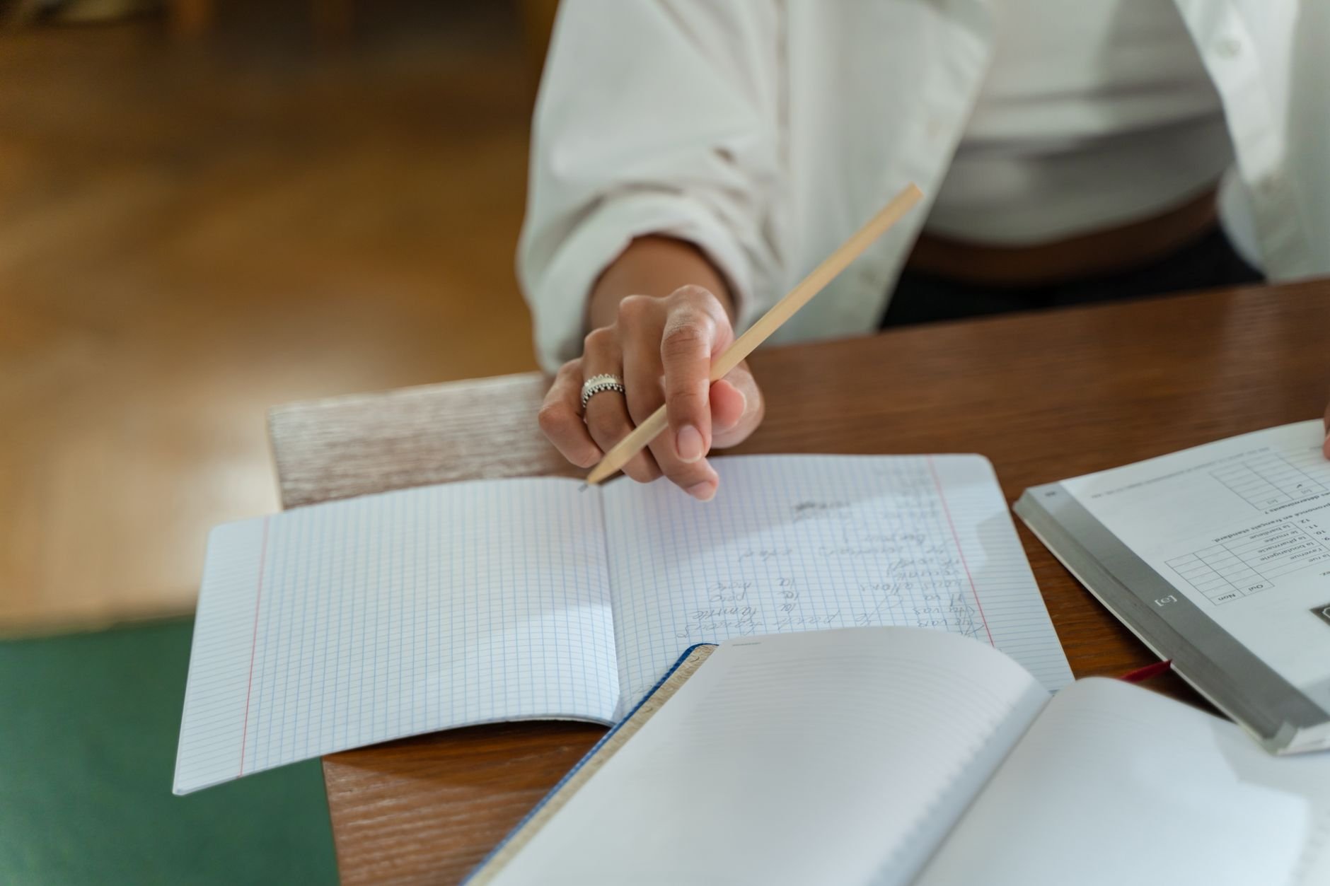 Primer plano de una mano con un lápiz sobre un cuaderno cuadriculado, en una mesa de madera.